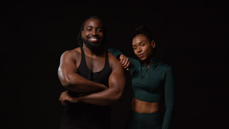 Retrato-De-Estudio-De-Una-Pareja-Atlética-Sonriente-O-Amigos-En-Ropa-Deportiva-Entrenando,-Fotografiados-Contra-Un-Fondo-Negro-2